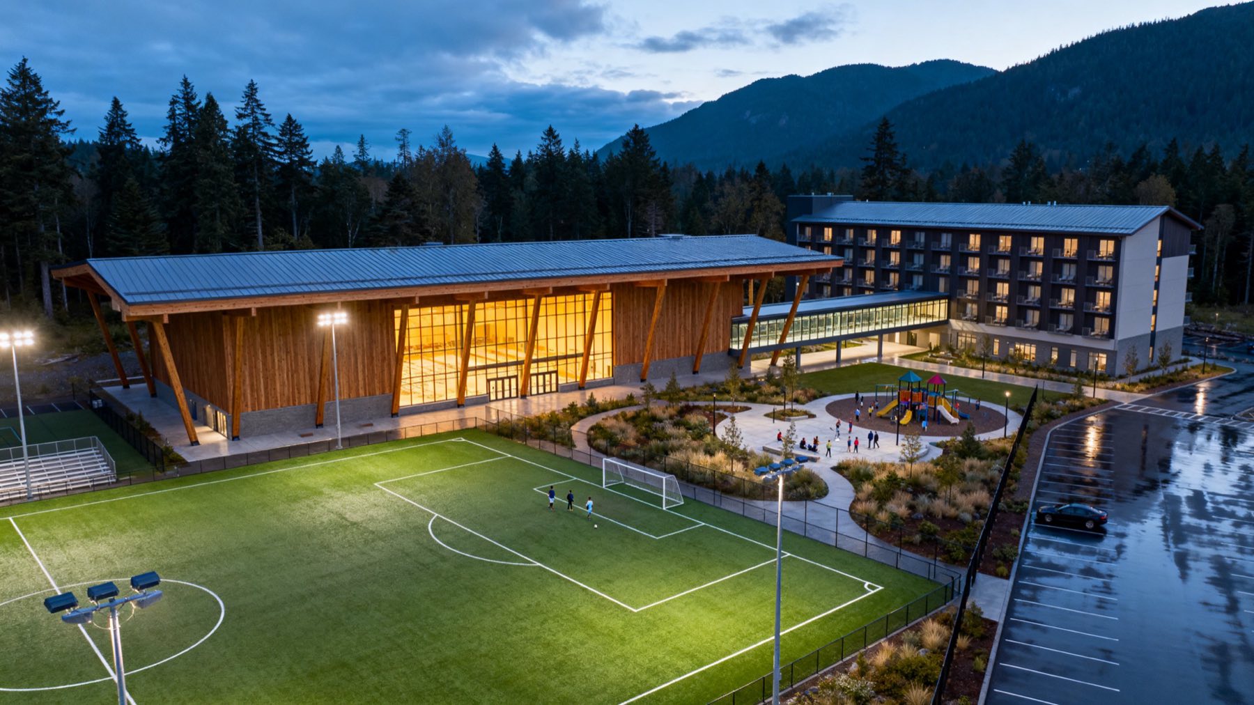 Concept illustration of an integrated sports, events and hospitality campus in a forested Vancouver Island valley at dusk
